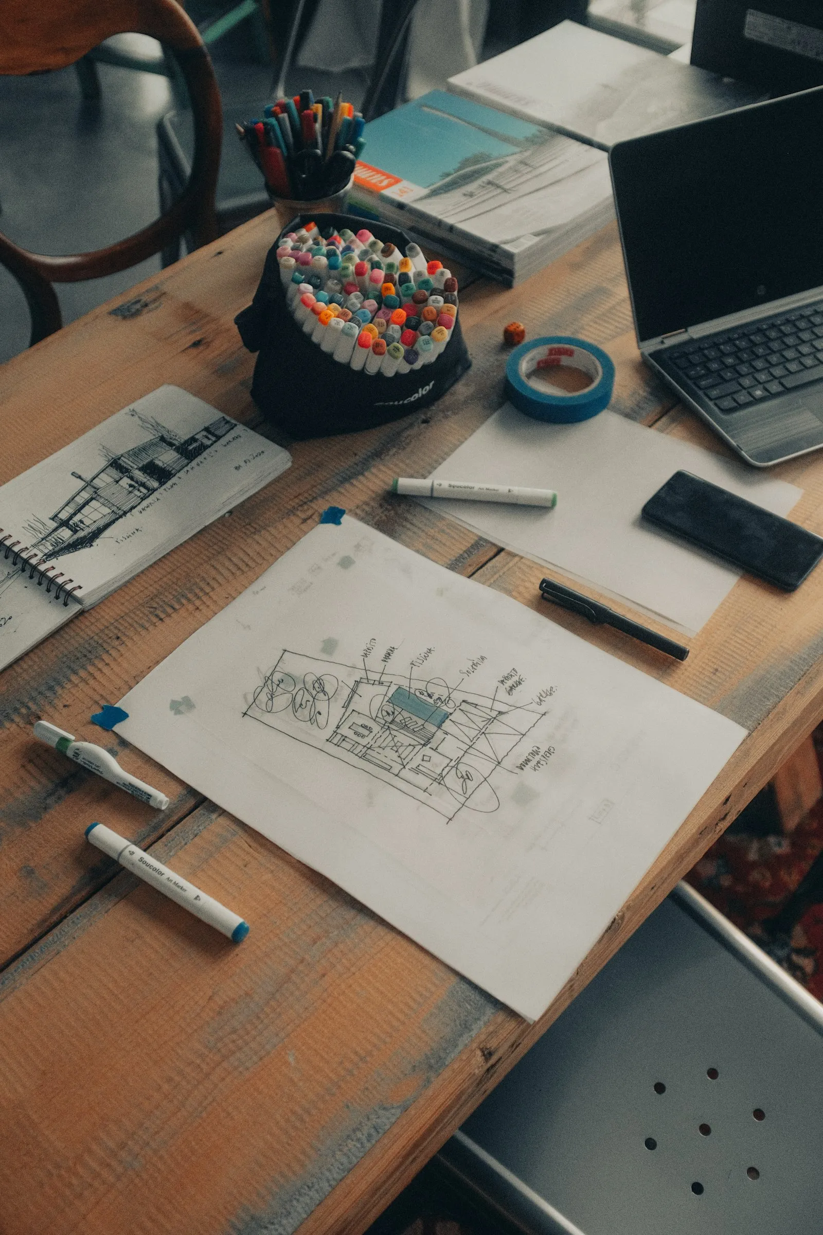 Meja kerja dengan sketsa denah rumah, penggaris, dan alat tulis arsitektur